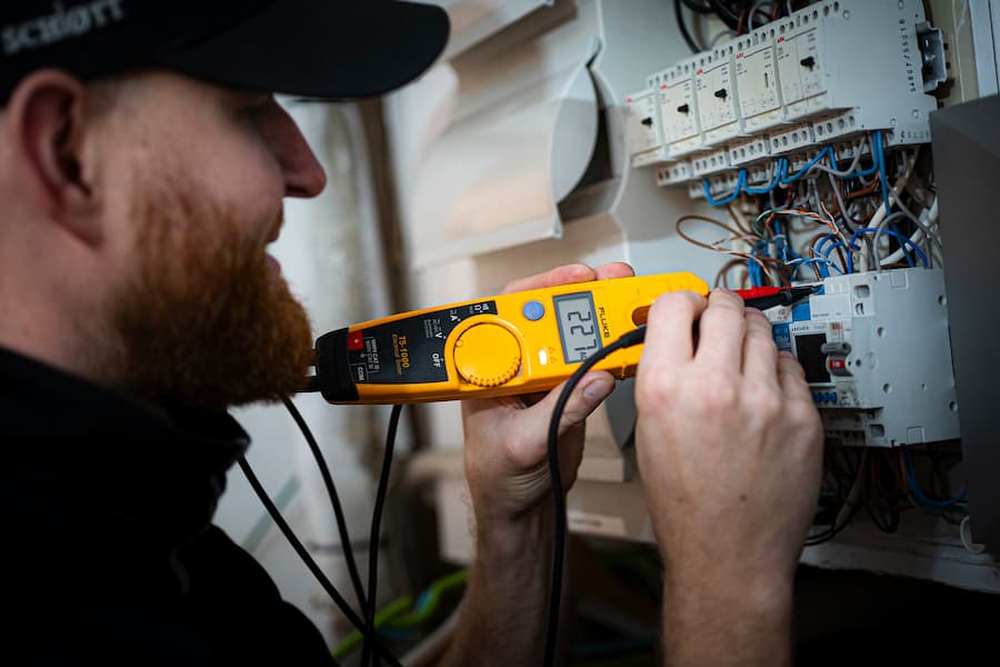 En elektriker udfører et el-tjek med et digitalt måleinstrument på en kompleks elinstallation i en bygning i København. Han kontrollerer spændingen og sikrer, at installationen fungerer korrekt. Billedet illustrerer professionelt tjek af elinstallation i København.